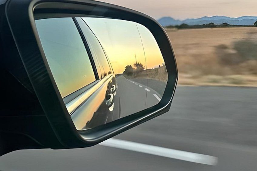 A side mirror of a car with a view of a highway and mountains in the distance. 2