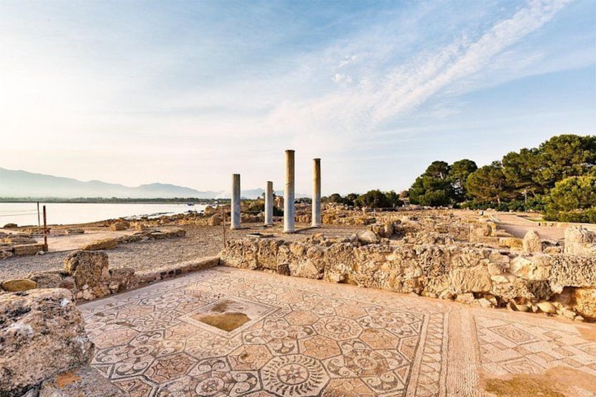 Ancient ruins with columns and patterned flooring near a body of water. 4