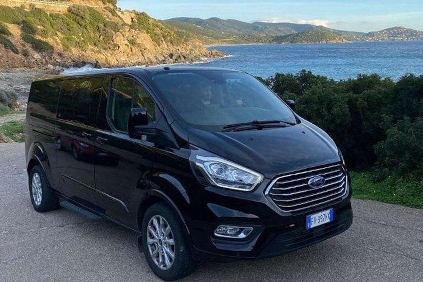 A black Ford Transit van parked on a coastal road with a scenic view of the sea and hills in the background. 2