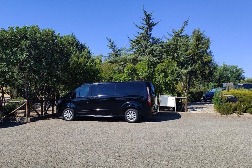 Un SUV negro estacionado en un aparcamiento de grava, con árboles y un cielo azul despejado al fondo. 2