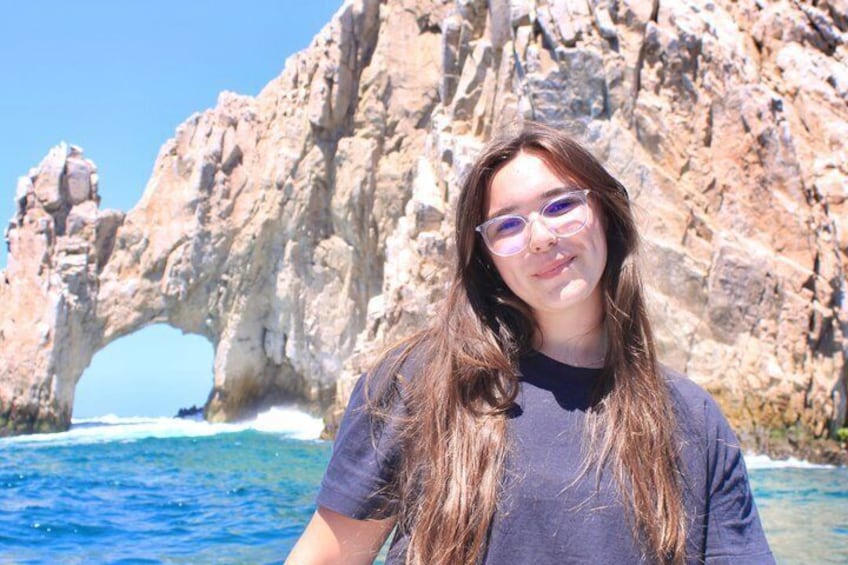 A person standing in front of a rocky coastal landscape with a prominent rock arch formation. 3