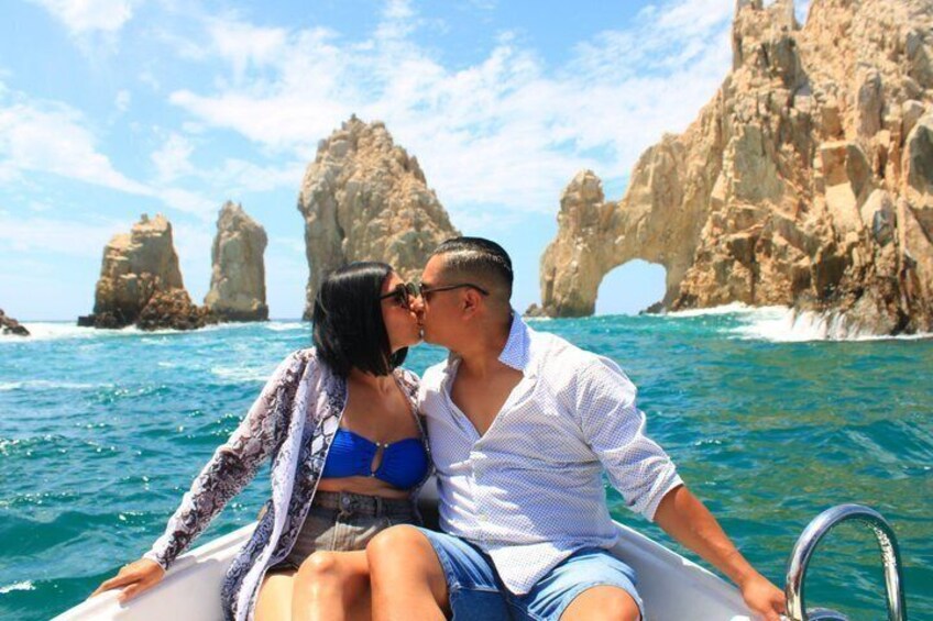 A couple on a boat with a rocky coastline and arch formations in the background. 2