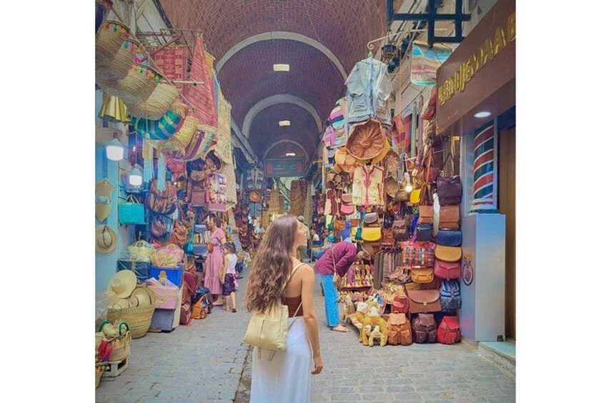 A narrow alley with colorful bags and baskets on display. 3