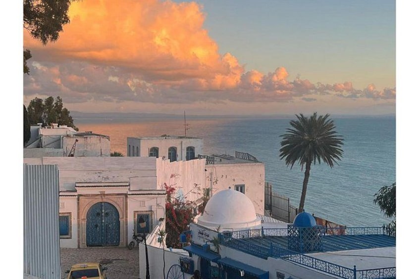 Une ville côtière aux bâtiments blancs, avec un palmier et un coucher de soleil sur la mer. 3