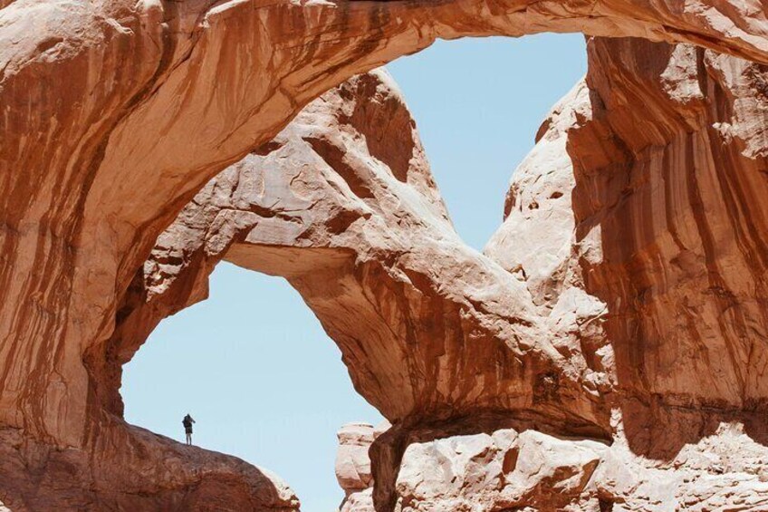 A natural rock arch formation with a person standing at its base. 2