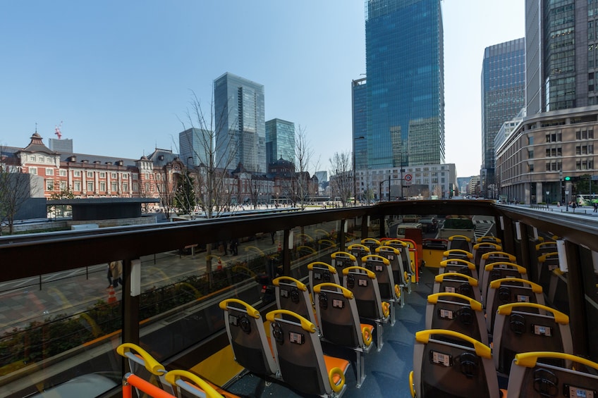 A bus with rows of seats, a cityscape with tall buildings, and a clear sky. 1