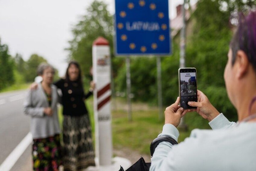 A person taking a photo with a smartphone, a blue sign with the European Union flag, and a red and white striped pole. 3