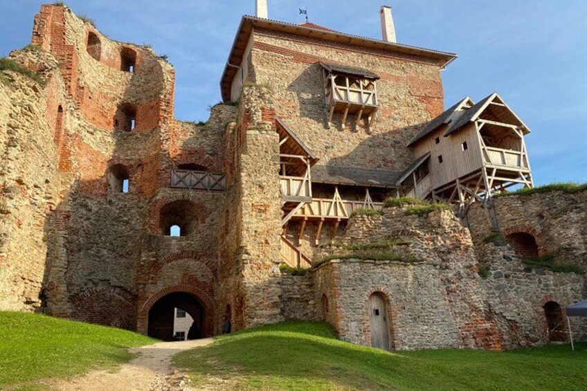 An ancient stone castle with wooden structures on top, a grassy foreground, and a clear sky. 2