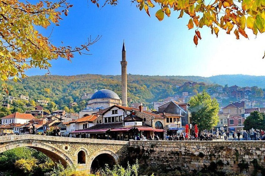 A stone bridge, a mosque with a dome and minaret, and a town with buildings and hills in the background. 5