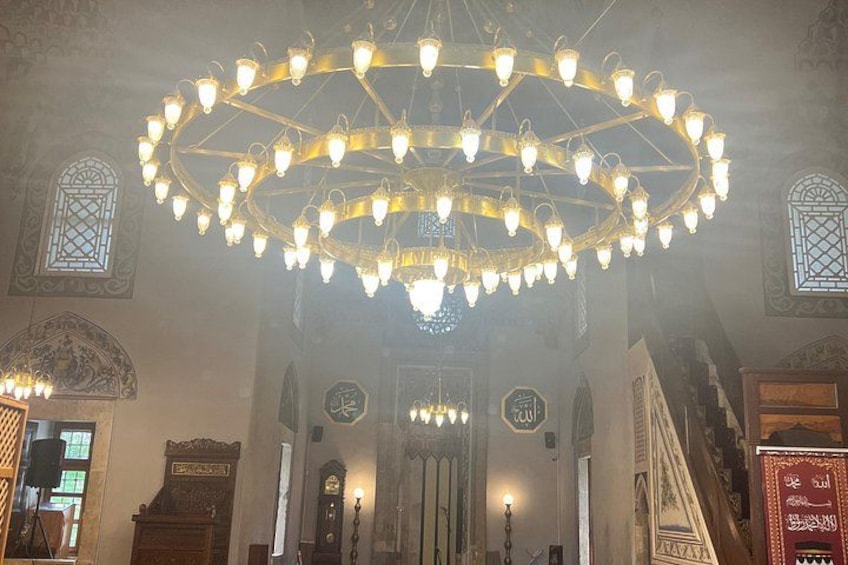 A grand hall with a large circular chandelier, ornate wooden furniture, and intricate wall designs. 3