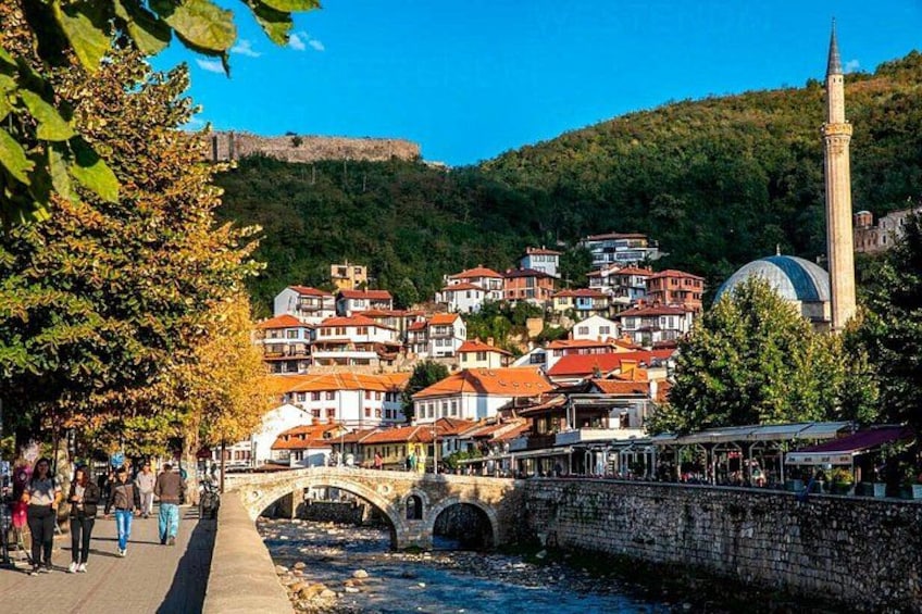 A river with a stone bridge, a mosque, and a hillside settlement with red-roofed buildings. 1