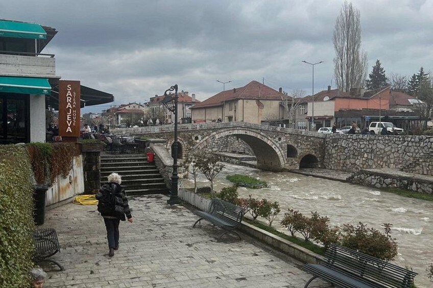 A stone bridge, a river, and a person walking on a cobblestone path. 4