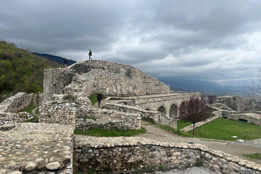 Ancient ruins with stone walls and arches, surrounded by grassy areas and hills in the background. 2