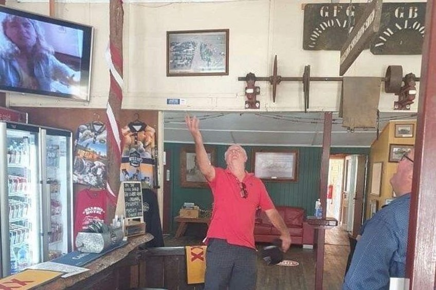 Un homme vêtu d’un t-shirt rouge est en train de soulever des poids dans une pièce où se trouvent un téléviseur, des affiches et un comptoir de bar. 2