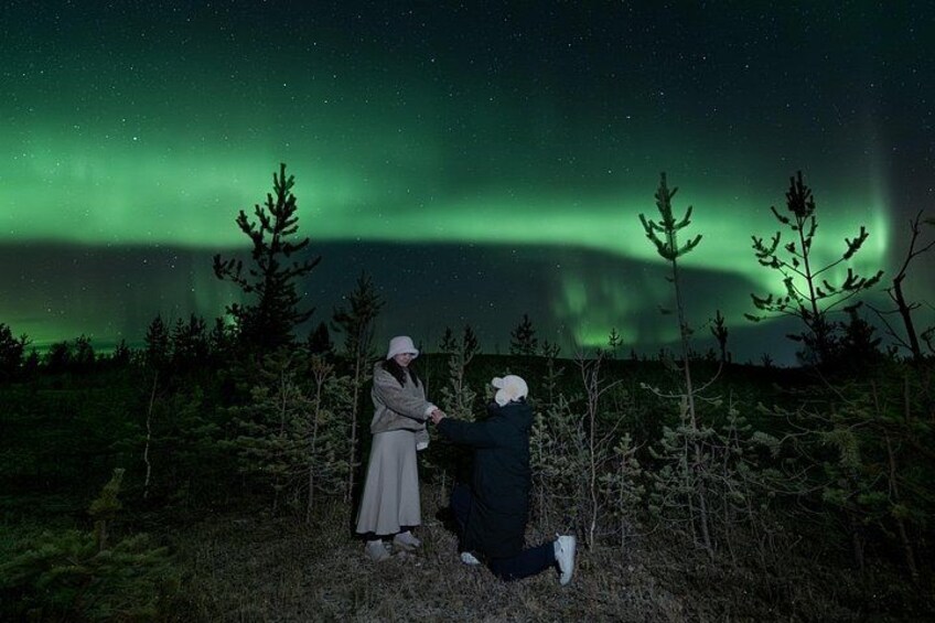 Two people in a forest with the Northern Lights in the background. 2