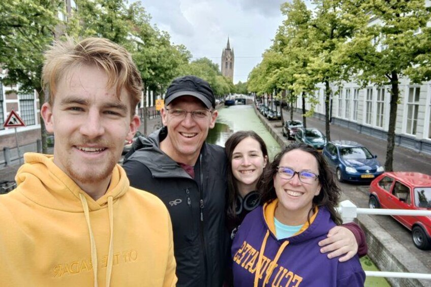A group of people standing on a street with trees and a building in the background. 2