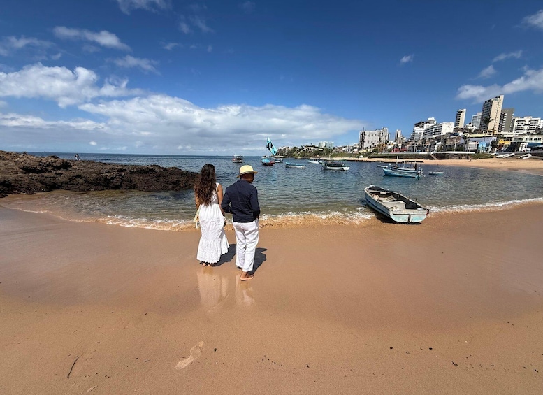 Una playa con gente caminando, barcos y un paisaje urbano al fondo. 2