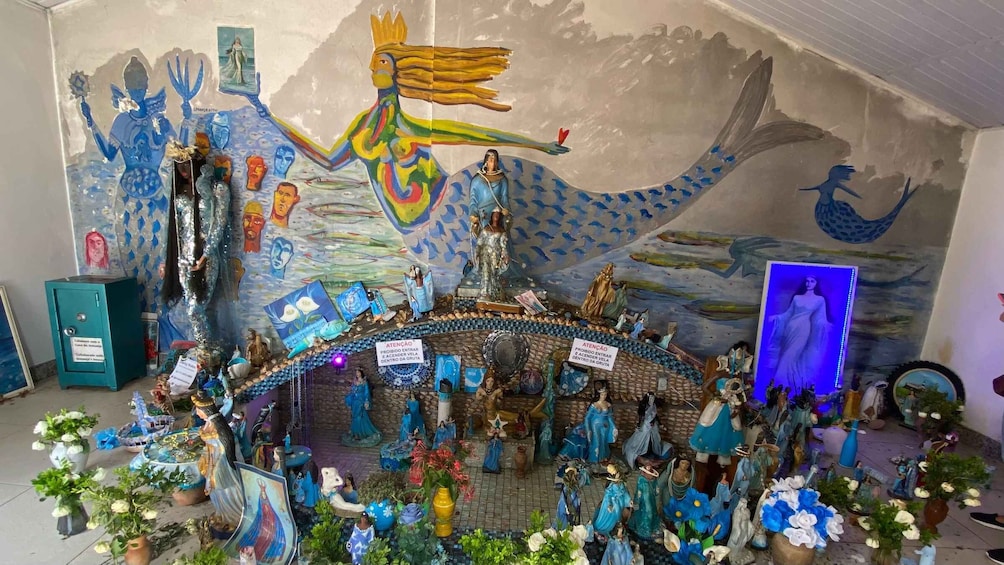 Un santuario con estatuas religiosas, flores y un mural. 1