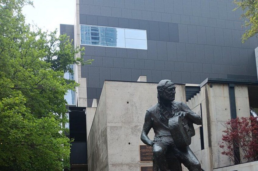 En staty av en person i en dynamisk pose, en modern byggnad med reflekterande fönster och ett träd med gröna löv. 2