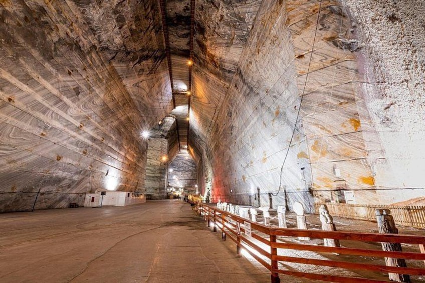En underjordisk tunnel med buet loft, træsøjler og gelænder langs stien. 2
