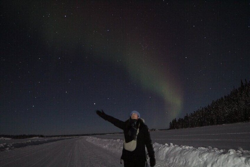 A person standing on a snow-covered road under a starry night sky with the aurora borealis visible. 4