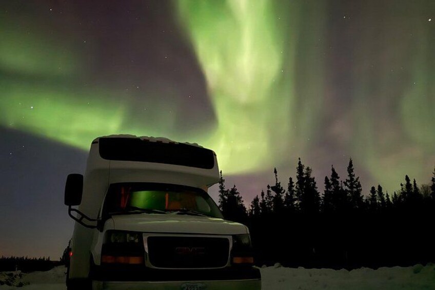 Una caravana blanca estacionada sobre nieve, con la aurora boreal al fondo. 2