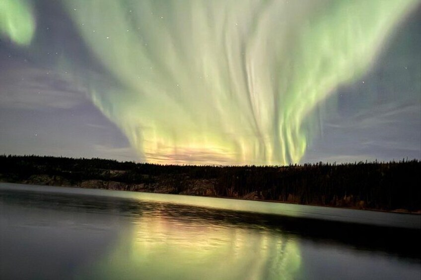 The Northern Lights over a calm lake with a forested shoreline. 2