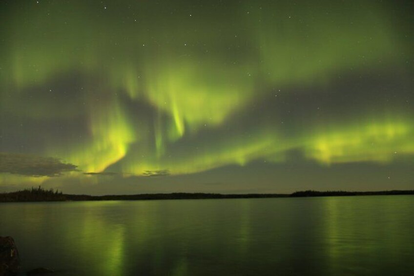 The Northern Lights over a calm lake with a forested shoreline. 5