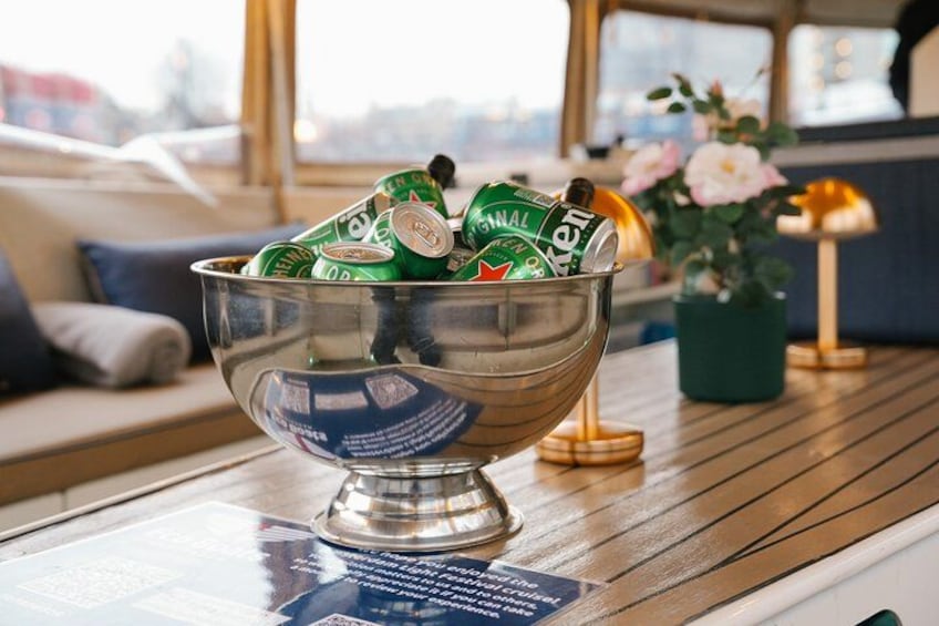 A metal bowl filled with beer cans on a wooden table. 3