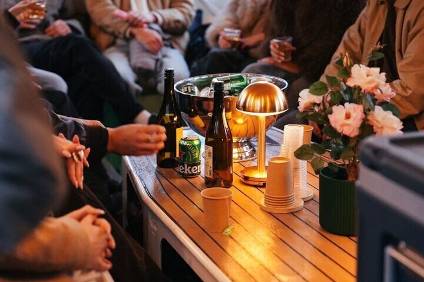 Un grupo de personas sentadas en una mesa de madera con bebidas, una lámpara y velas. 4