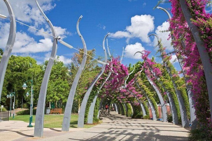 A pathway lined with metal arches and pink flowering vines. 1