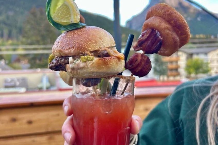 En person holder en drink med en burger og en croissant ovenpå. 4