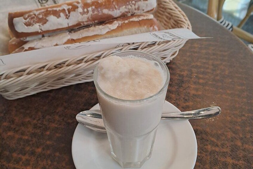 Un vaso de leche con una cuchara sobre un platito, una cesta de pan y una cesta de mimbre al fondo. 5