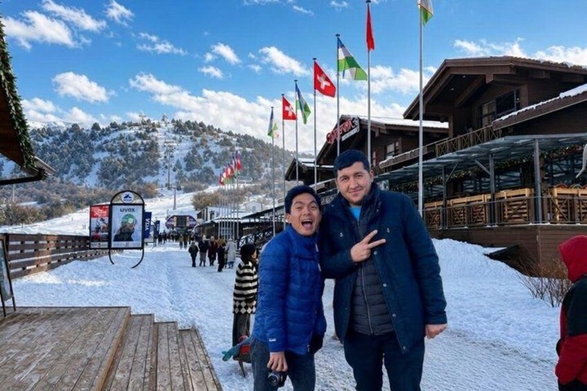 A snowy mountain path with flags, a wooden deck, and a building with a balcony. 2