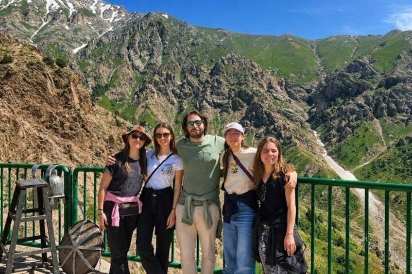 Un groupe de personnes se tient sur une rambarde verte, avec un paysage montagneux en arrière-plan. 5