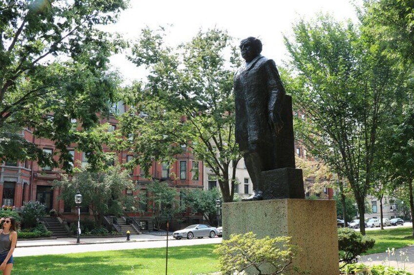 Una estatua de un hombre sobre un pedestal en un parque con árboles y un edificio al fondo. 4