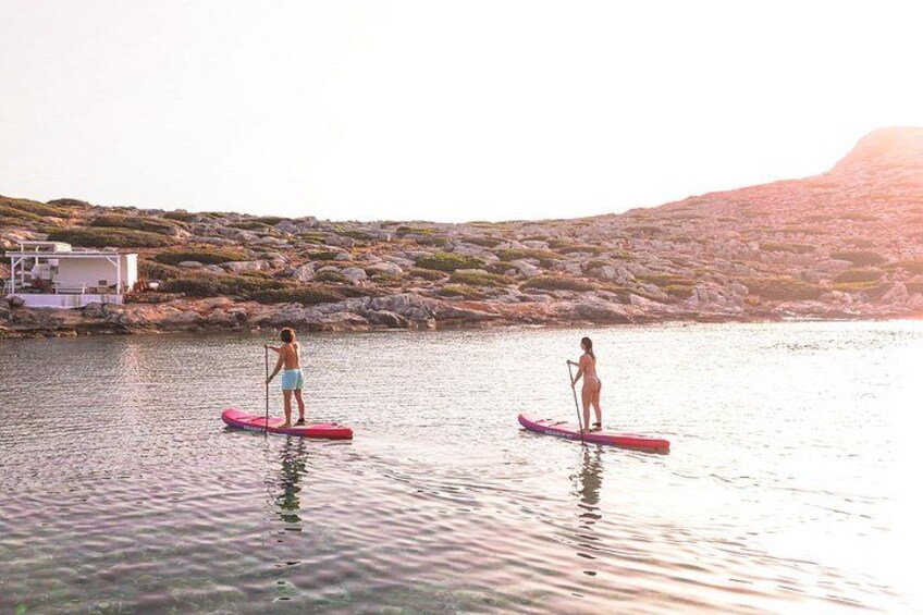 Zwei Personen stehen auf Paddleboards auf ruhigem Wasser, im Hintergrund eine felsige Uferlinie und eine Bootsanlegestelle. 3