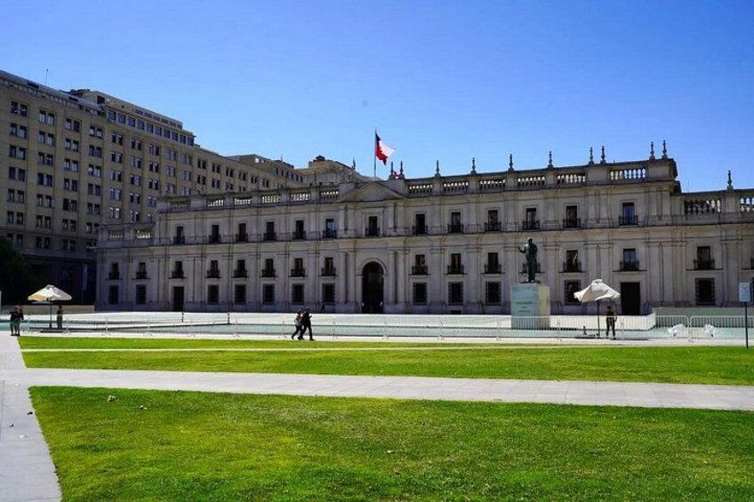 Un edificio histórico grande con una bandera, una estatua y un césped bien cuidado. 3