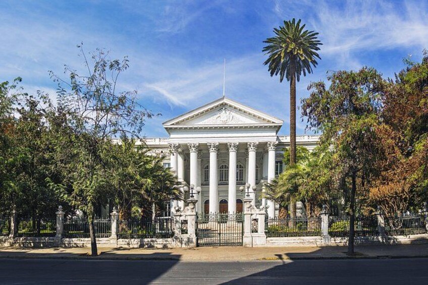 Un edificio neoclásico con columnas, una palmera y una valla. 5