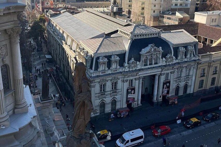 A historic building with classical architecture, a statue, and a busy street with cars and pedestrians. 2