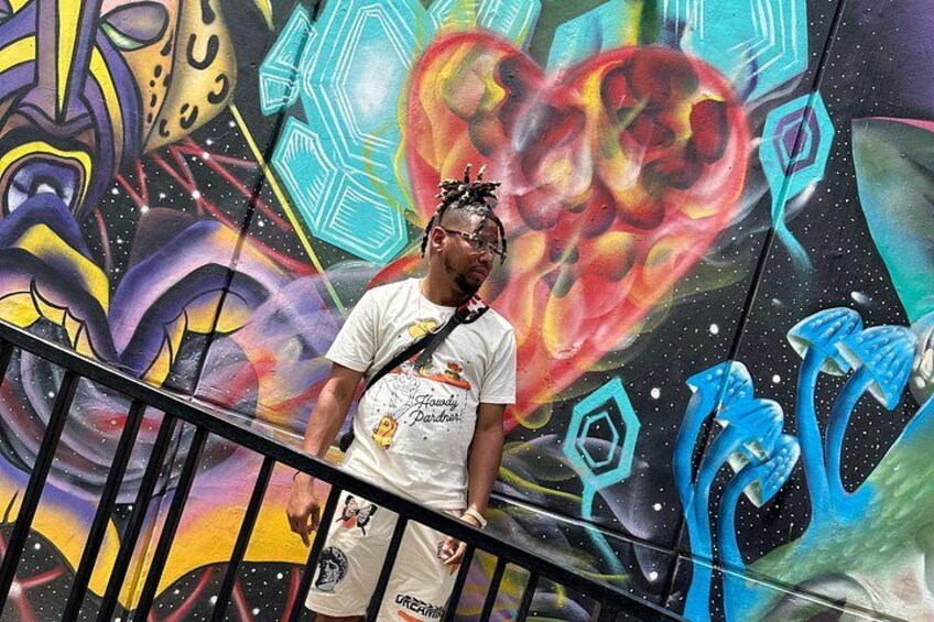 Une personne se tient sur un escalier mécanique, avec une fresque murale colorée, ornée de graffitis, en arrière-plan. 2