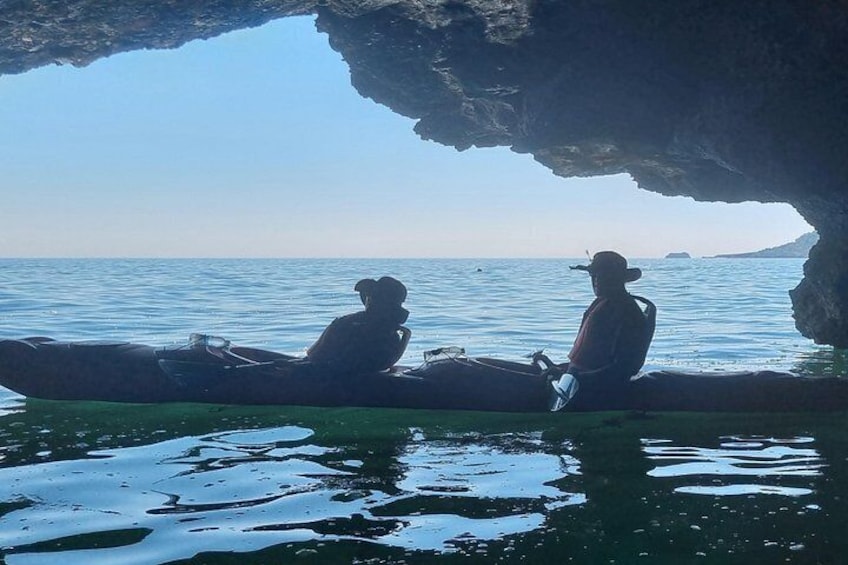 Two people in a kayak under a cave entrance with the sea in the background. 4