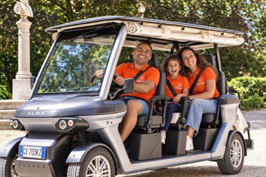 A golf cart with three people wearing orange shirts. 1
