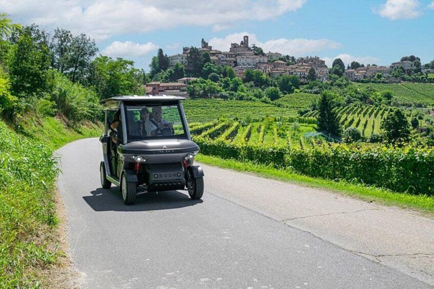 A golf cart on a rural road with vineyards and a historic town in the background. 2