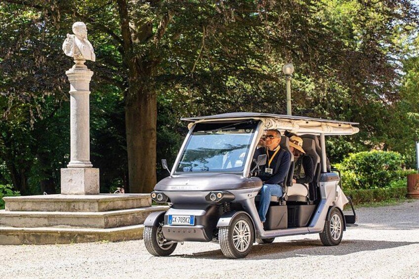 A golf cart with two passengers, a statue, and trees in the background. 3