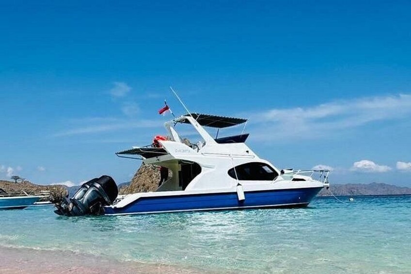 A white and blue boat with a flag on the back, docked at a beach with clear water and distant mountains. 3