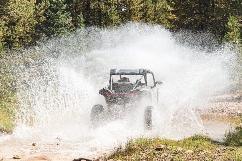 A vehicle driving through a shallow body of water, creating a large splash. 2