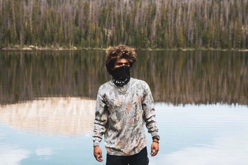 A person standing by a calm lake with a forest in the background. 3