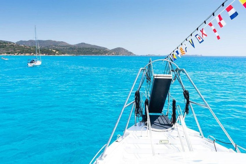 A boat with a clear view of the turquoise sea, a sailboat in the distance, and a mountainous coastline. 4
