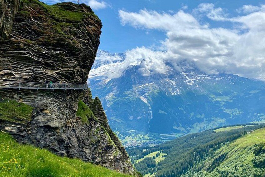 A mountain landscape with a narrow bridge, lush green valleys, and snow-capped peaks. 2